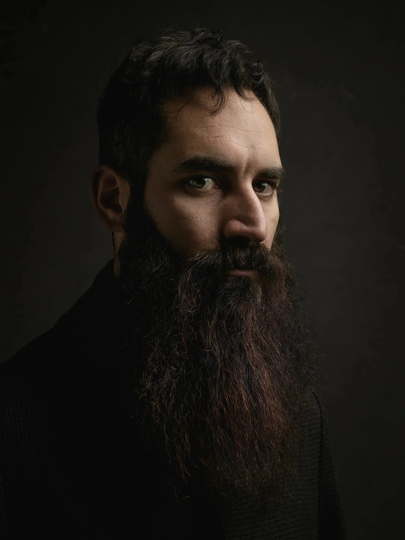 Side profile close-up portrait of a man with a very long dark beard.